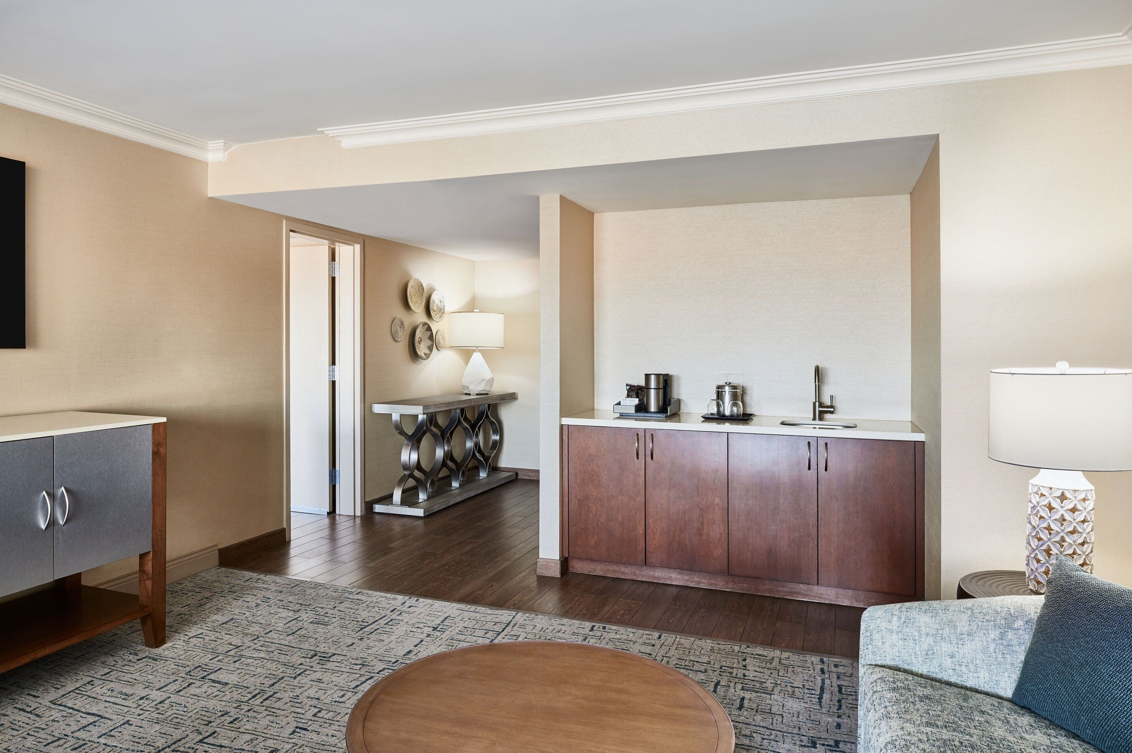 Ein Hotelzimmer mit Holzboden, einer Couch, einem kleinen runden Tisch, einer Küchenzeile mit Kaffeemaschine und einer Lampe.