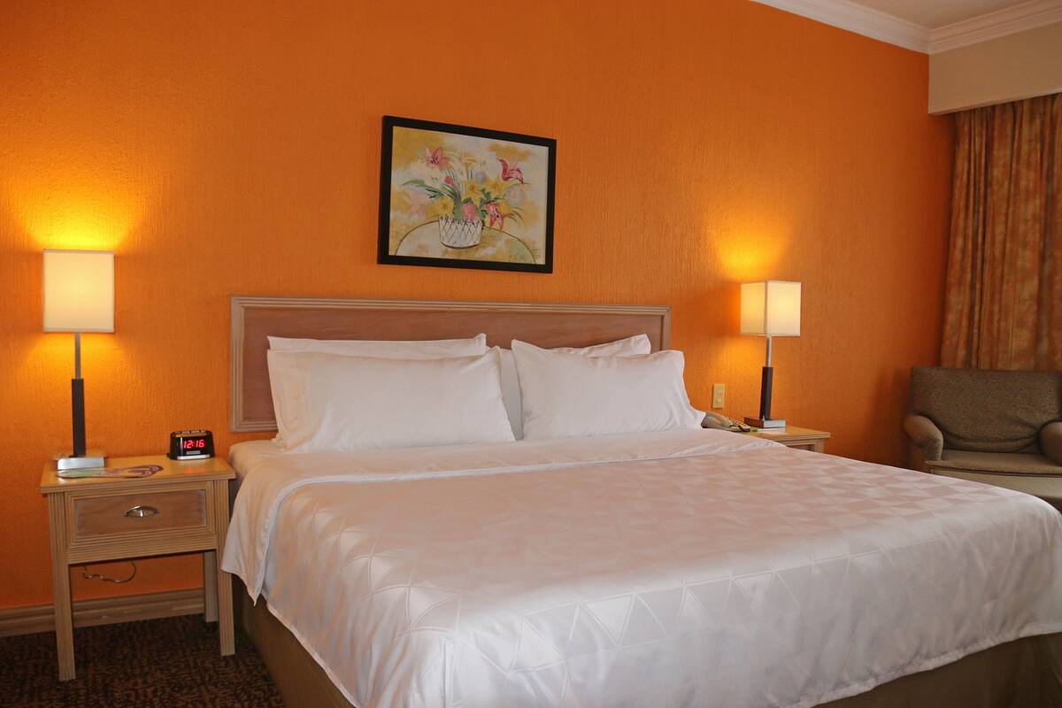 Une chambre d’hôtel avec un grand lit, deux lampes de chevet, une table de chevet avec une horloge et un tableau au mur.