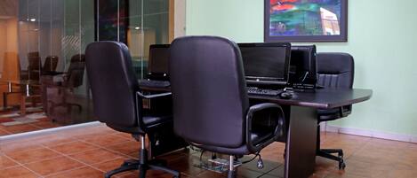 A conference room with two black office chairs, a desk with two laptops, and a framed abstract painting on the wall.