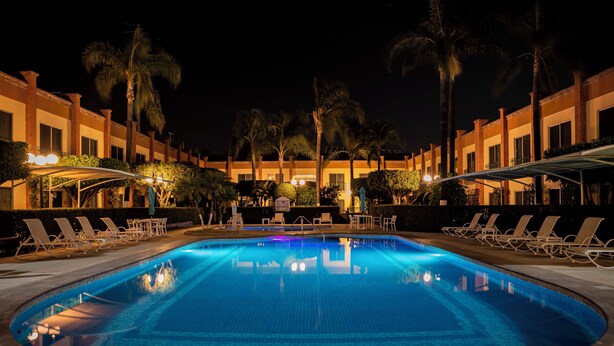 A swimming pool surrounded by lounge chairs and palm trees, with a building in the background. - Holiday Inn La Piedad by IHG (La Piedad)