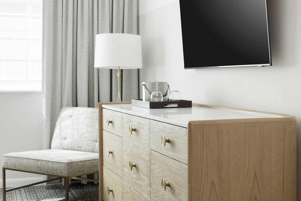 Una habitación de hotel moderna con un aparador de madera, un televisor de pantalla plana, una lámpara y una silla.