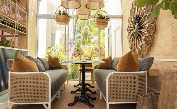 A cozy seating area with wicker chairs and a round table, a wall-mounted tennis racket display, and a view of lush greenery outside. - Kimpton Surfcomber Hotel by IHG (Miami Beach)