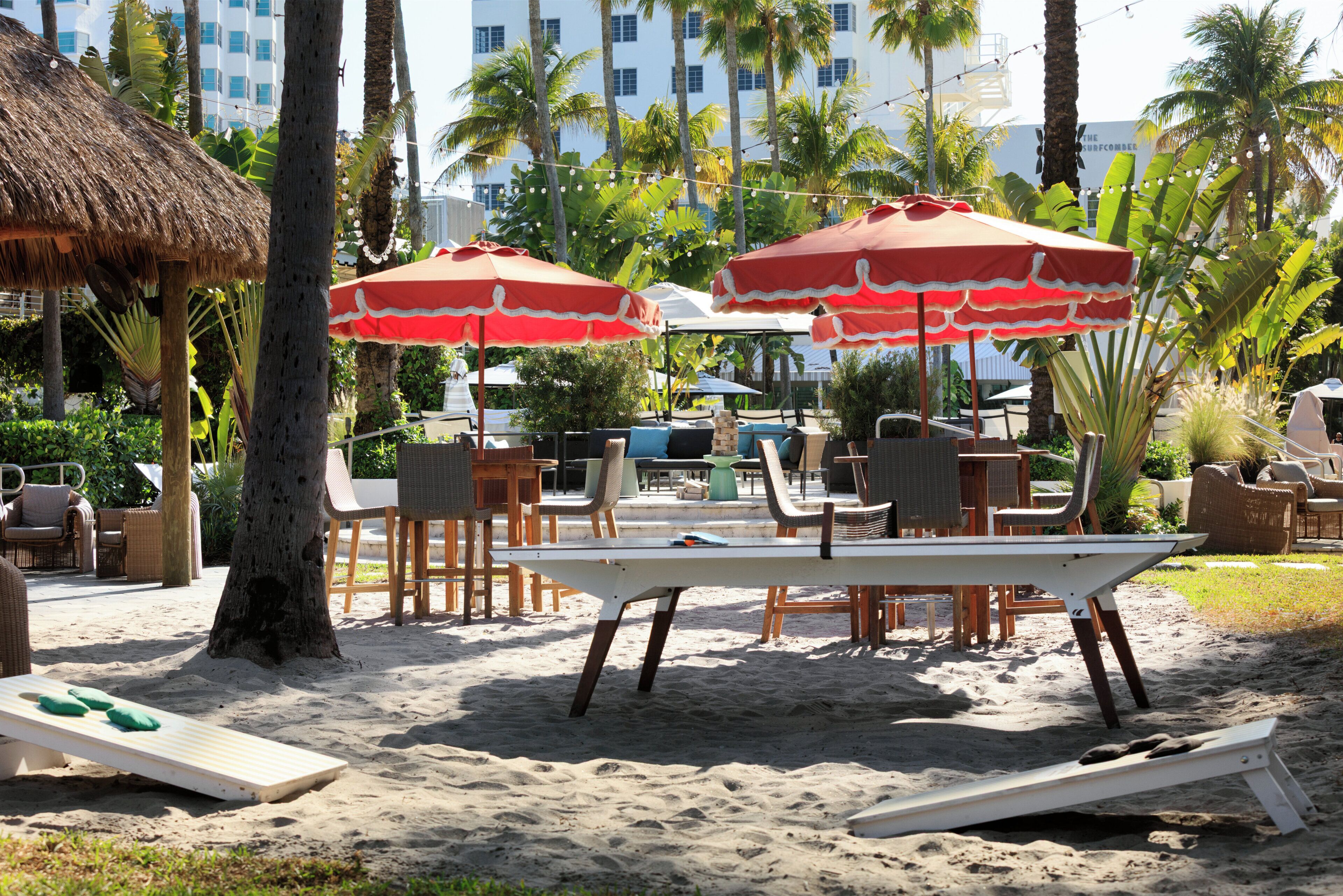 A beachside lounge area with thatched umbrellas, wooden lounge chairs, and a white table.