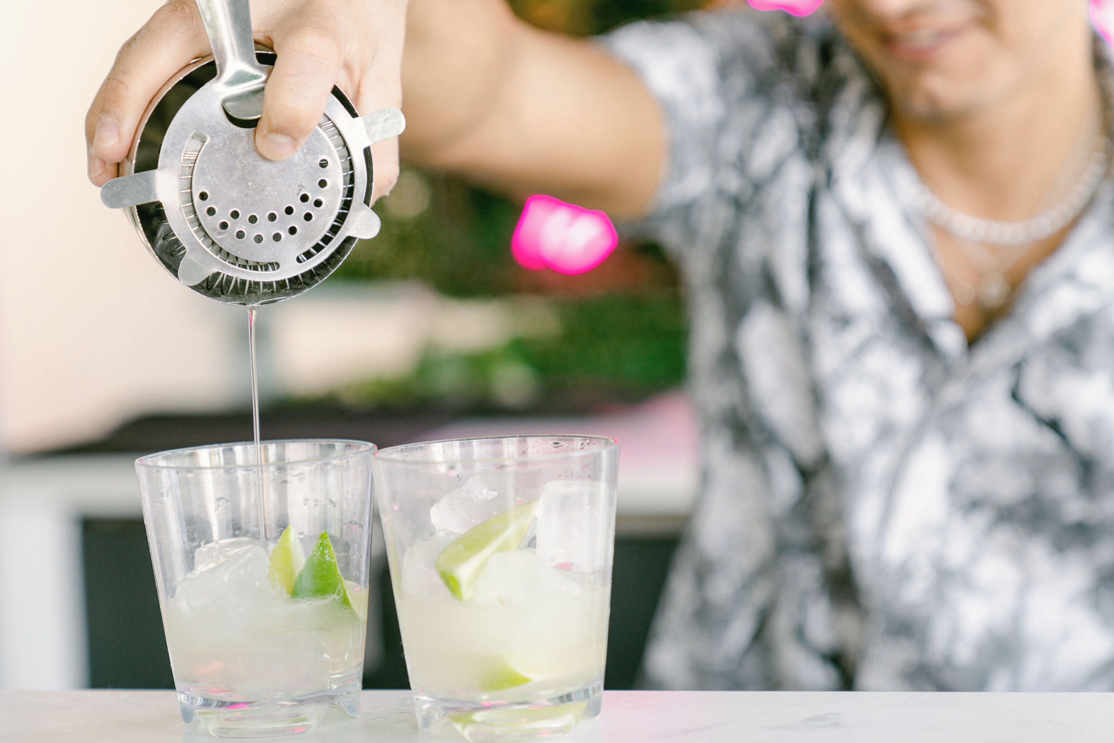 A person pouring a clear liquid into a glass with ice and lime.
