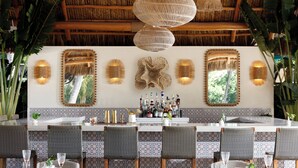 A bar area with a long counter, multiple chairs, and a decorative wall with mirrors and lights. - Kimpton Surfcomber Hotel by IHG (Miami Beach)