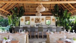 An outdoor restaurant with thatched roof, wicker furniture, and a central bar area. - Kimpton Surfcomber Hotel by IHG (Miami Beach)