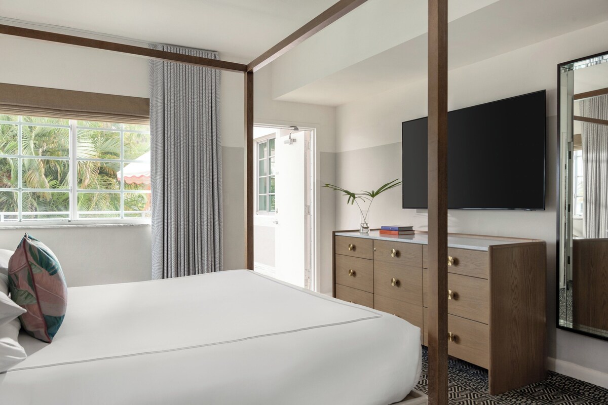 A hotel room with a large bed, a wooden dresser, a flat-screen TV, and a window with curtains.