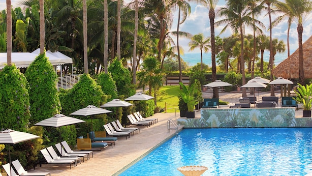 A poolside area with lounge chairs and umbrellas, surrounded by palm trees and a view of the ocean. - Kimpton Surfcomber Hotel by IHG (Miami Beach)