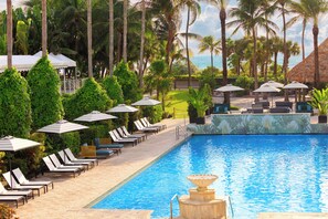 A poolside area with lounge chairs and umbrellas, surrounded by palm trees and a view of the ocean. - Kimpton Surfcomber Hotel by IHG (Miami Beach)