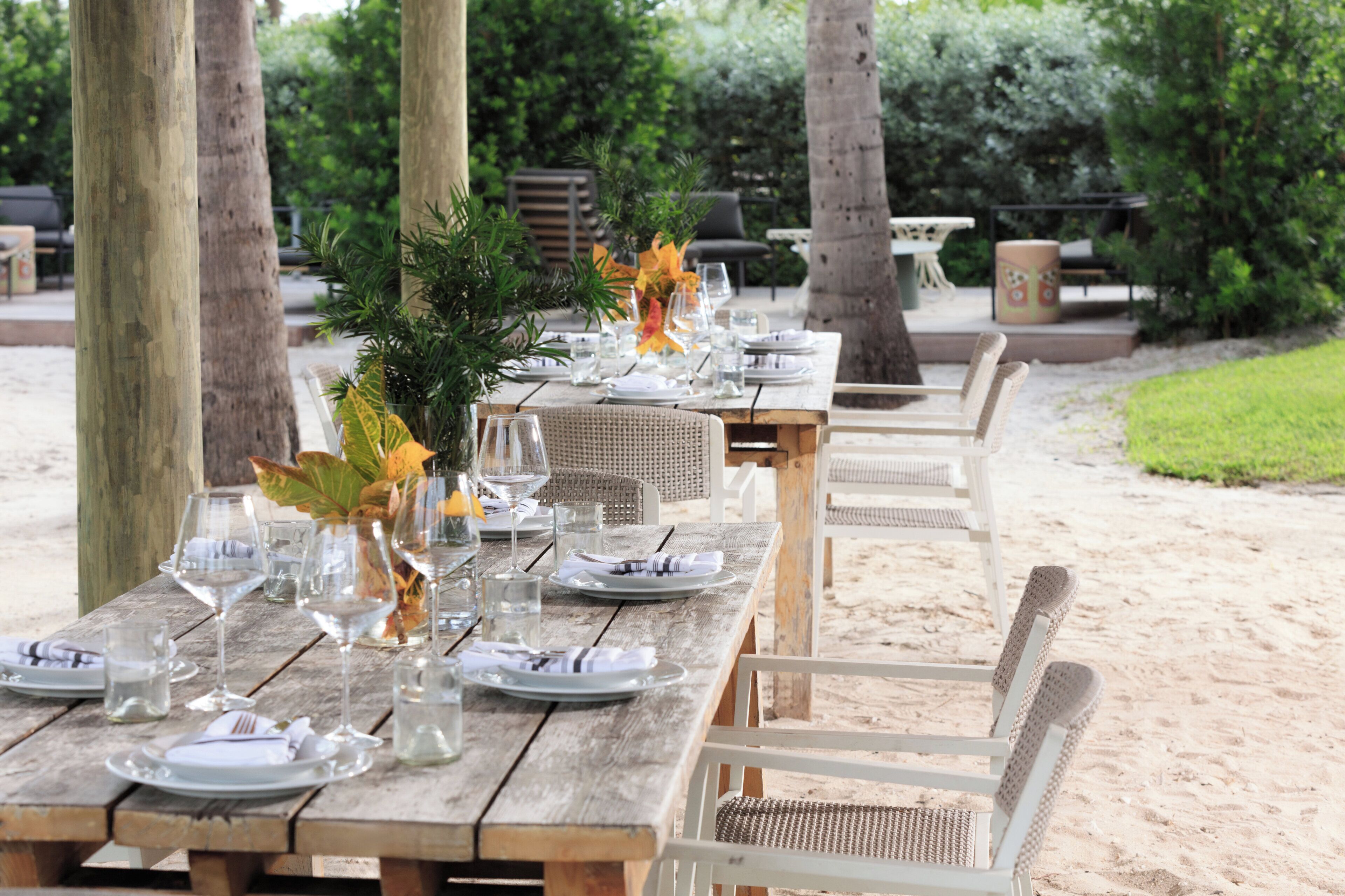A wooden outdoor dining table set with plates, glasses, and cutlery, surrounded by wicker chairs.