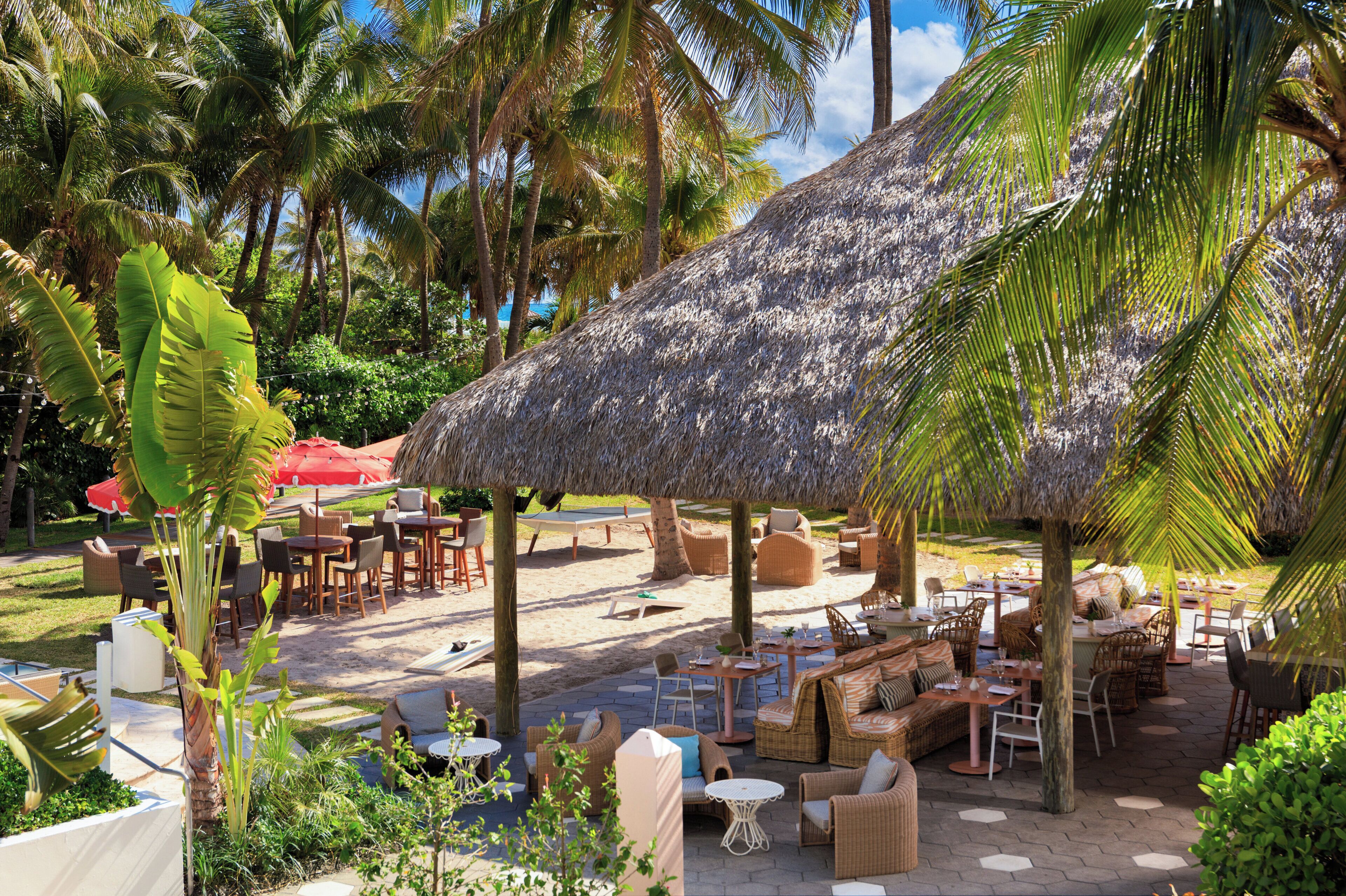 An outdoor seating area with thatched umbrellas, wicker furniture, and palm trees.