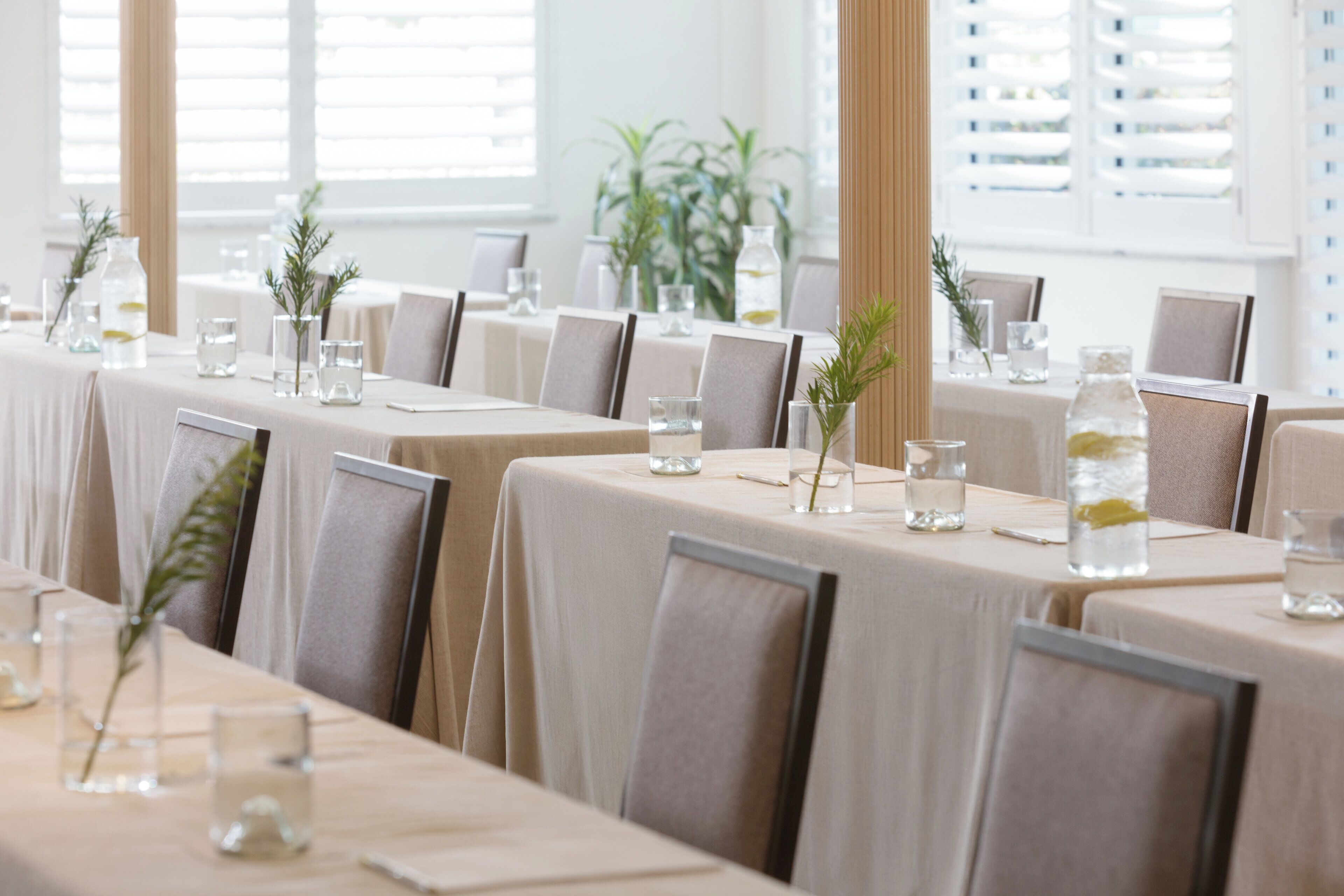 A long dining table set with chairs, water glasses, and small potted plants.
