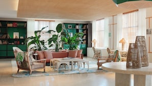 A spacious living room with a sofa, chairs, a coffee table, and a bookshelf. - Kimpton Surfcomber Hotel by IHG (Miami Beach)