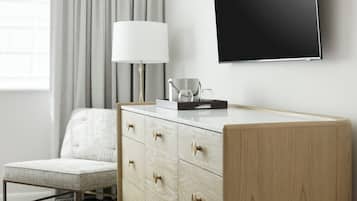 A modern hotel room with a wooden dresser, a flat-screen TV, a lamp, and a chair.