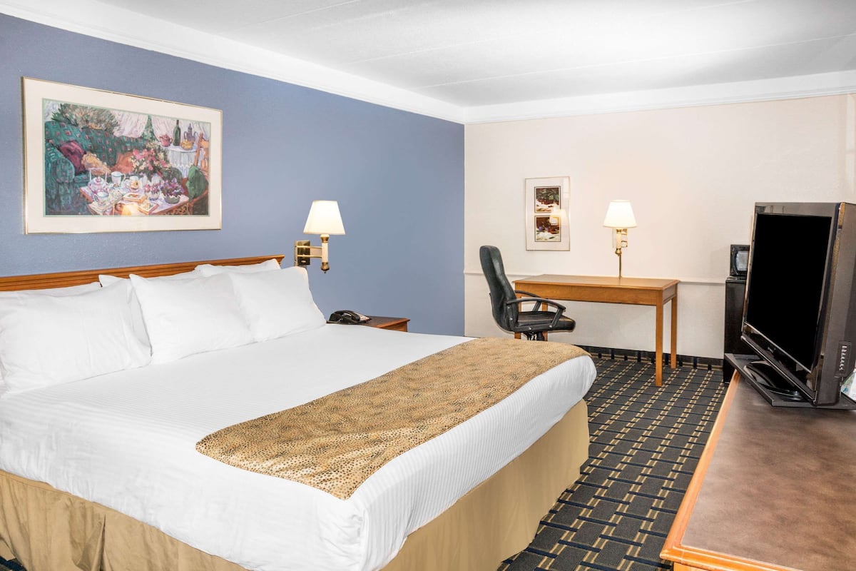 A hotel room with a bed, a desk, a television, and two wall-mounted lamps.