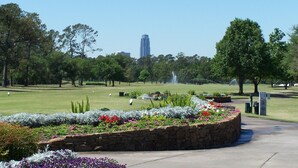 A park with a fountain, stone walls, and a clear view of a tall building in the distance. - Days Inn by Wyndham Houston (Houston)