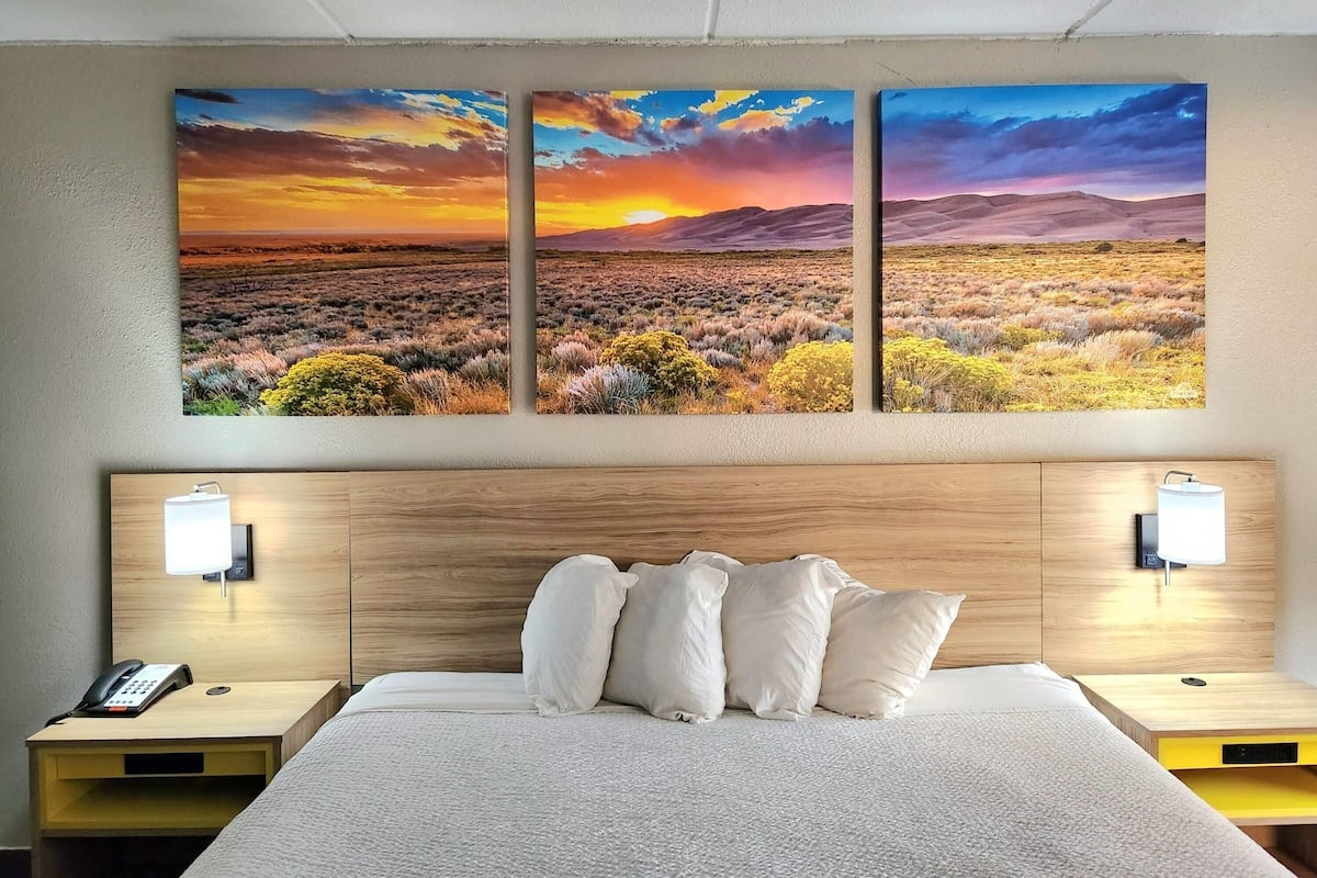 A hotel room with a large bed, two bedside tables, a nightstand, and a wall-mounted lamp.