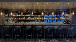 Eine Bar mit mehreren Regalen voller Spirituosenflaschen, einer Theke und einigen Barhocker.