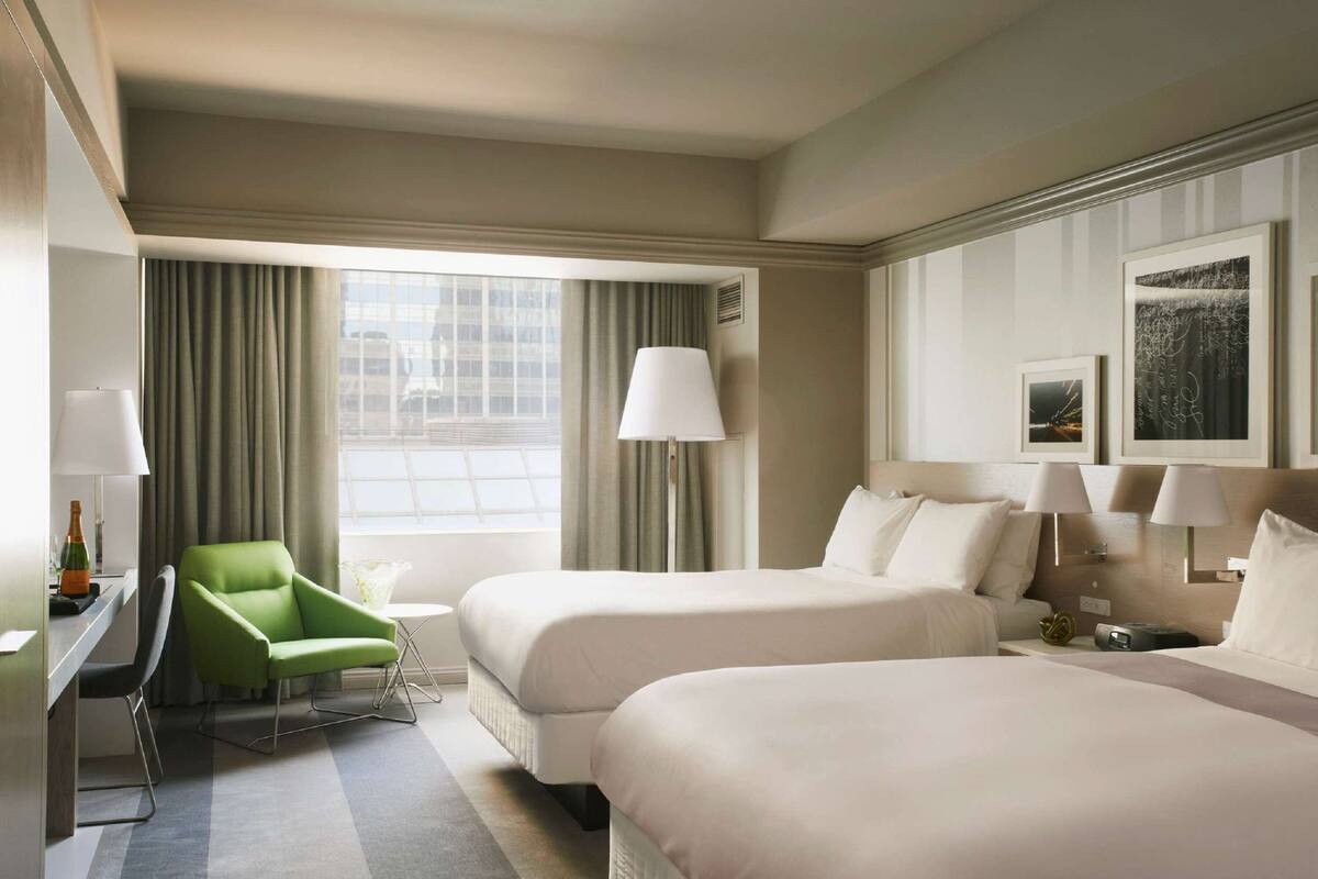 A hotel room with two beds, a desk, a chair, a lamp, and a window with curtains.