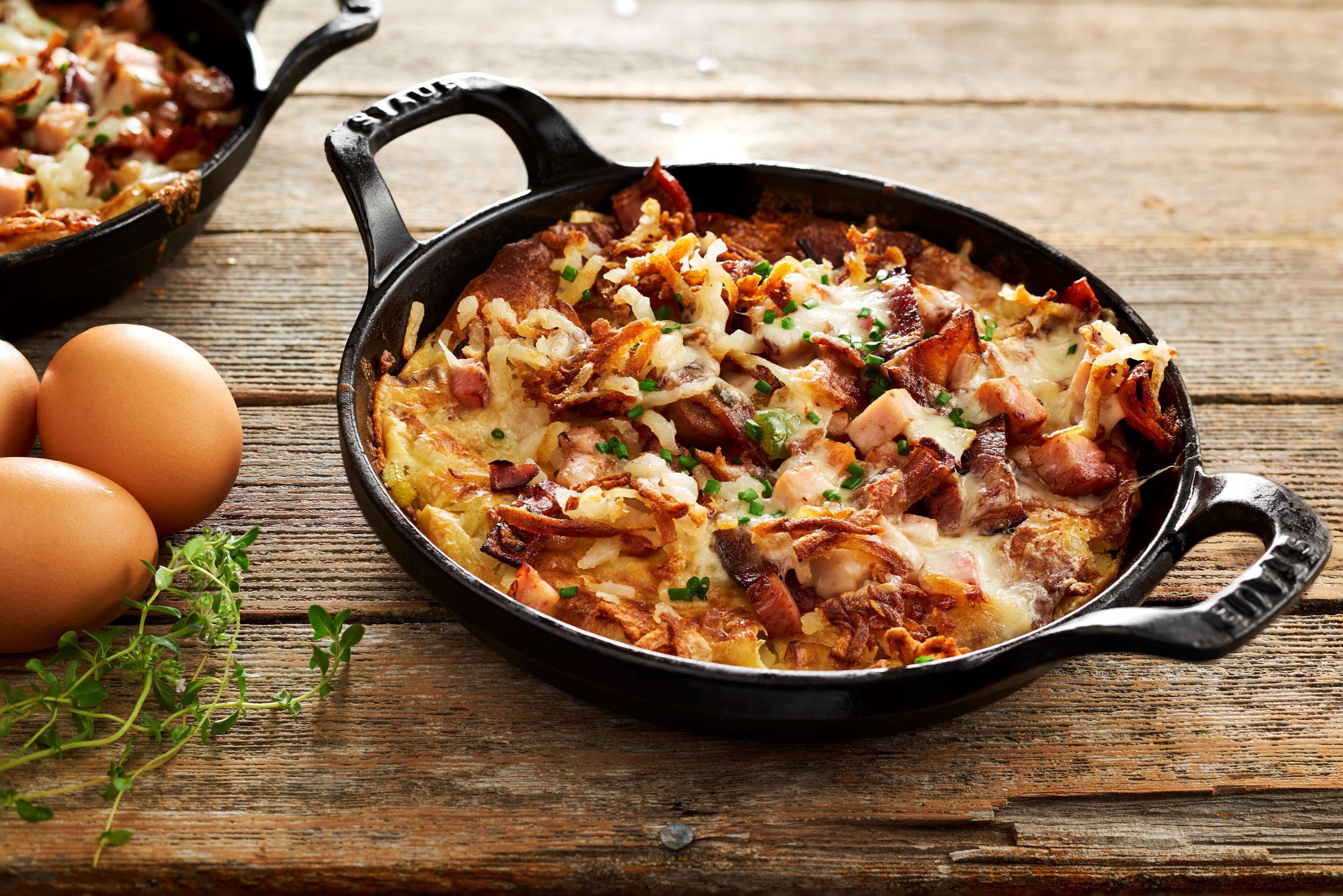 Une poêle contenant un plat composé d’œufs, de bacon et de fromage, posée sur une surface en bois.