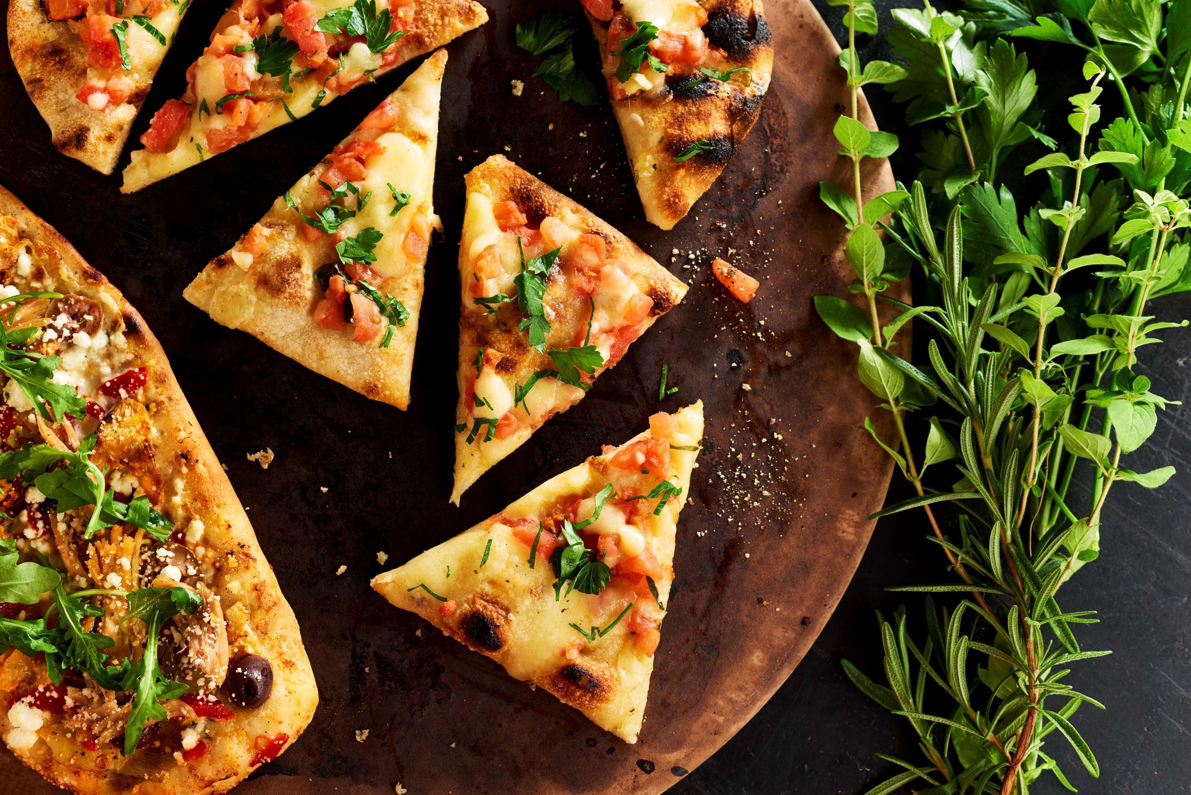 Una tabla de madera con varias porciones triangulares de pizza cubiertas de queso, tomates y hierbas.