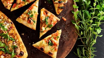 Una tabla de madera con varias porciones triangulares de pizza cubiertas de queso, tomates y hierbas.