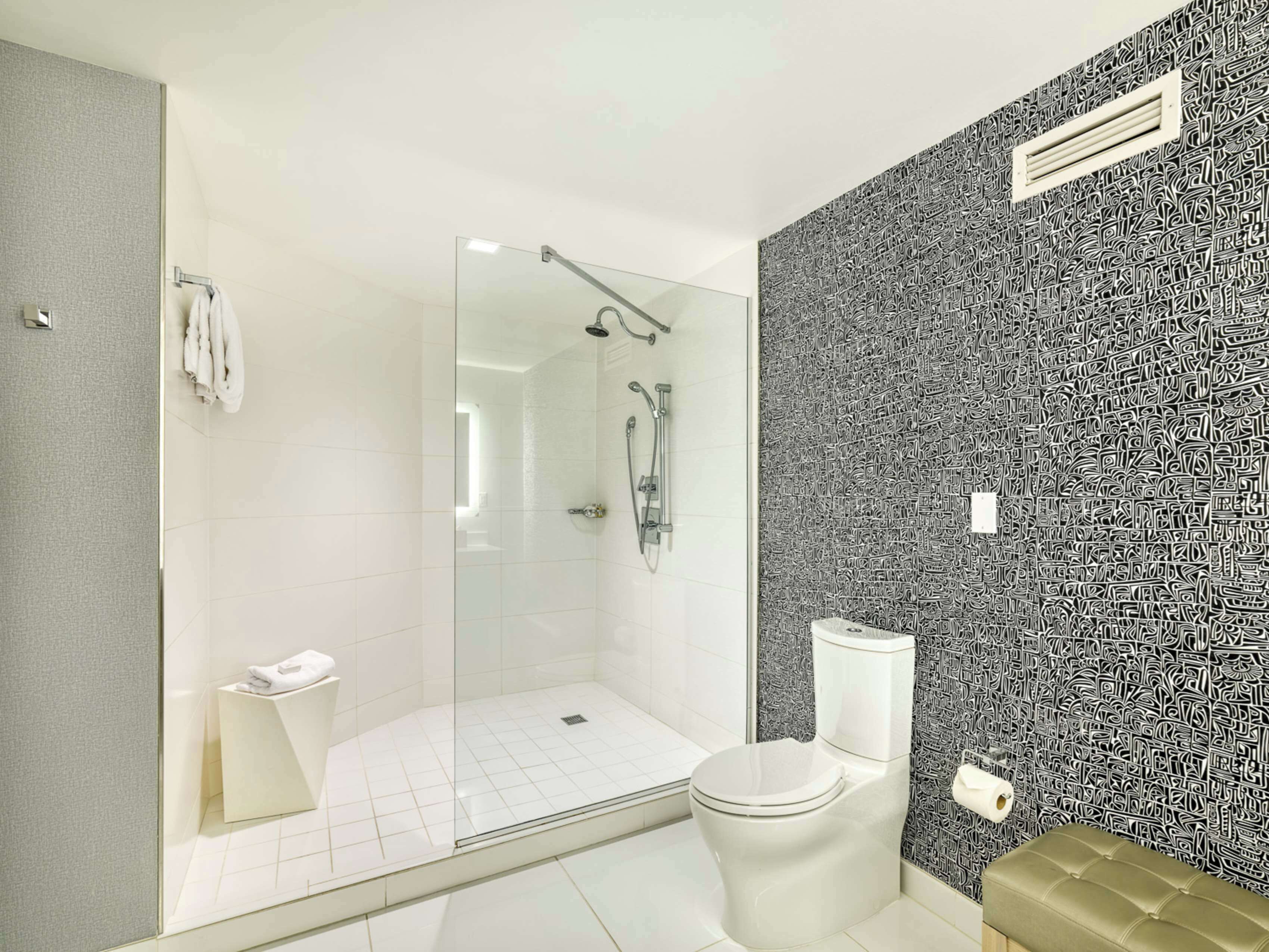 A modern bathroom with a glass-enclosed shower, a toilet, and a patterned wall.