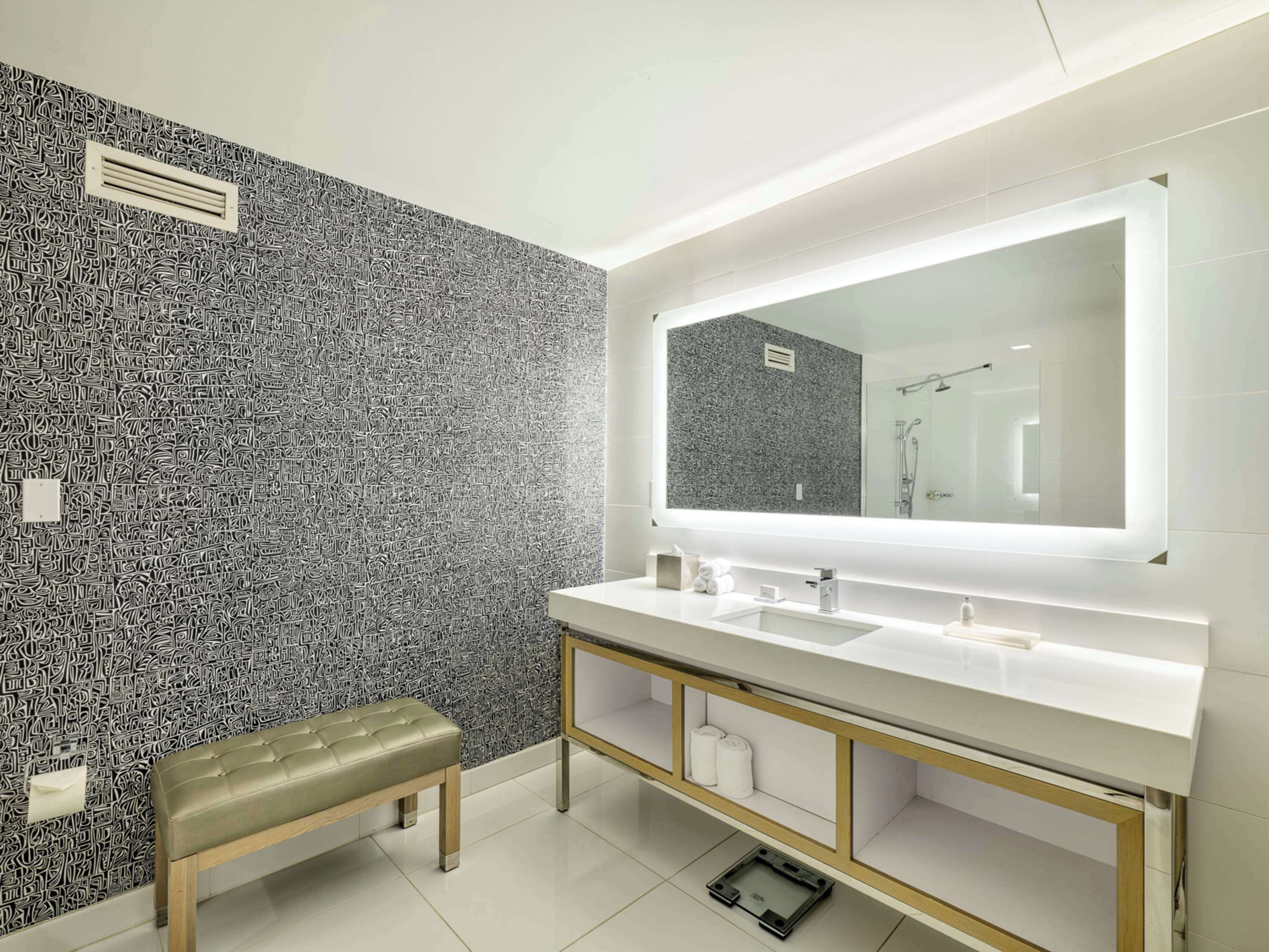 Ein modernes Badezimmer mit einem großen Spiegel, zwei Waschbecken, einer Sitzbank und einer Wand mit Muster.