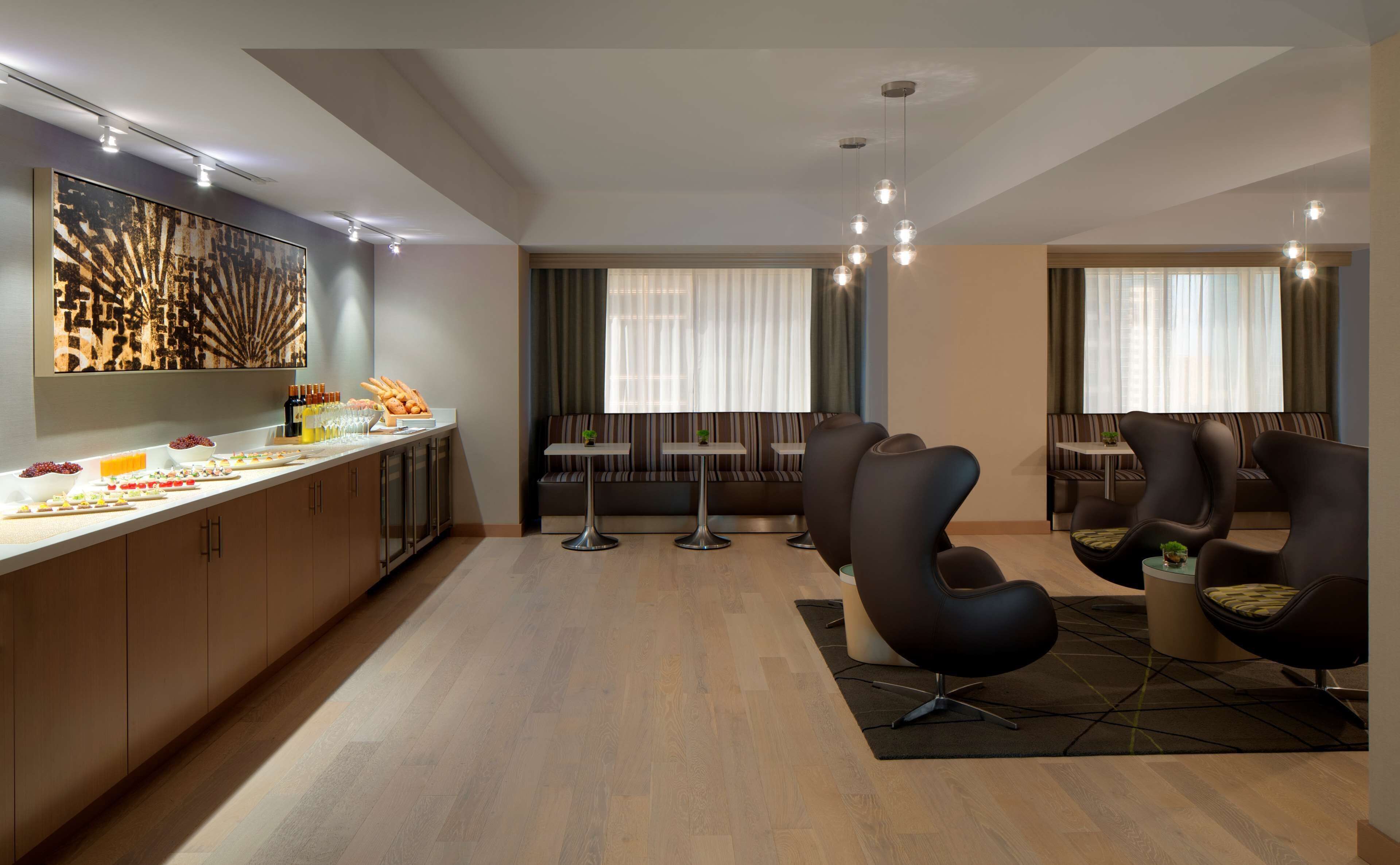 Moderni hotellihuone, jossa on aamiaisbuffet, oleskelualue ja suuret ikkunat.