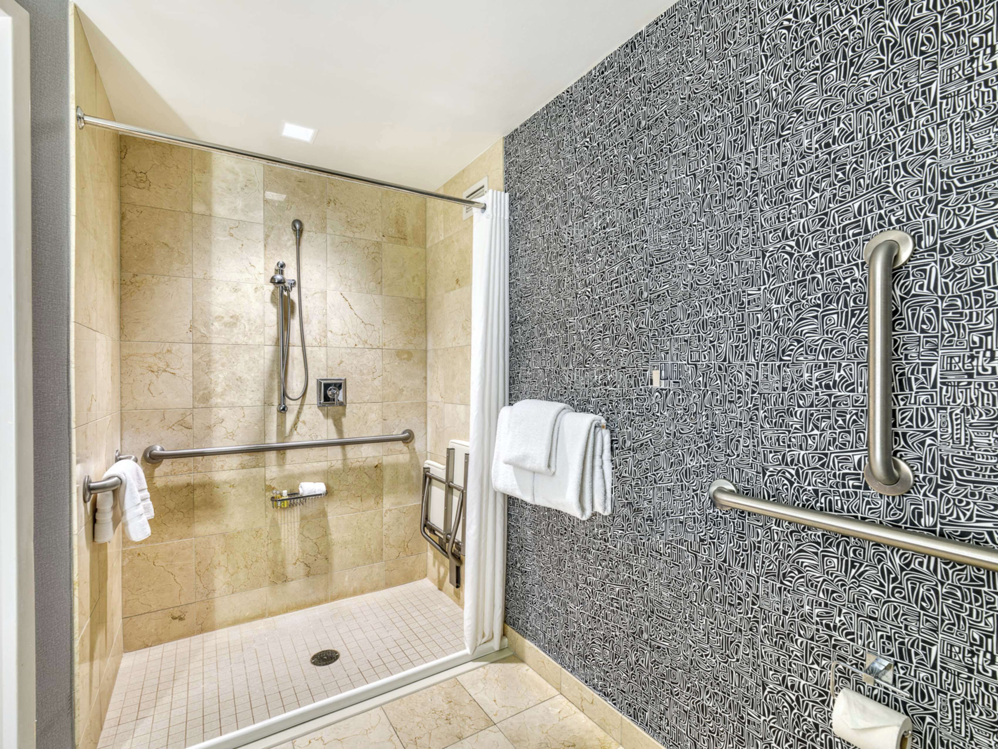 A modern bathroom with a glass-enclosed shower, a handrail, and a patterned wall.