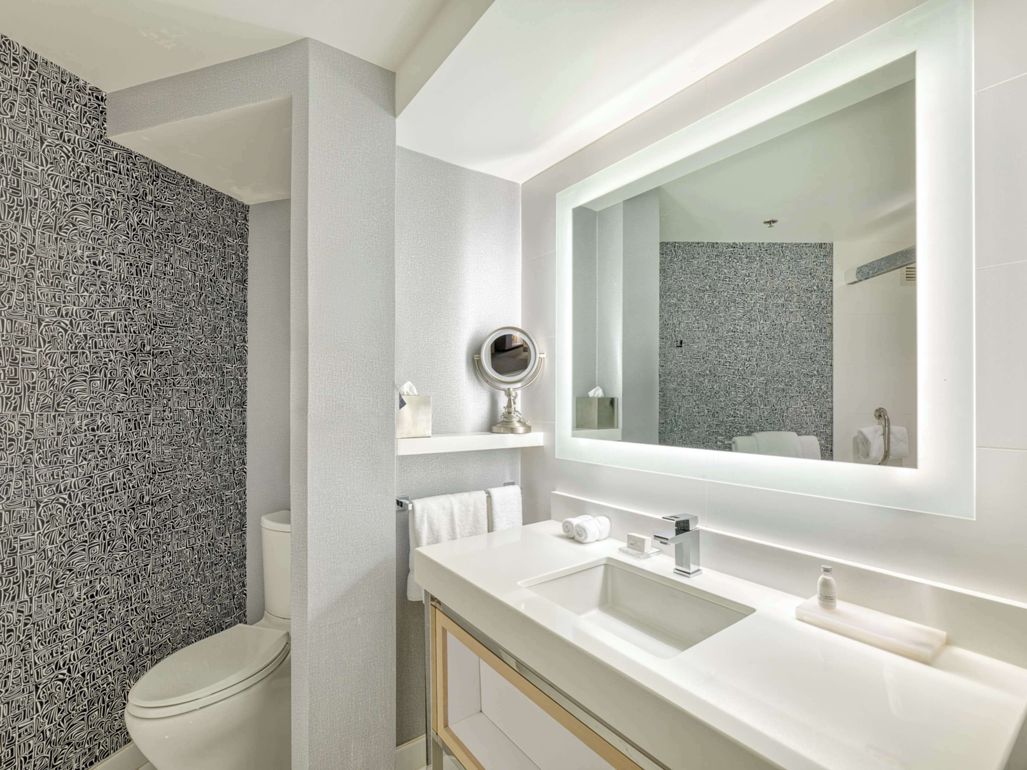 A modern bathroom with a large mirror, a sink, and a toilet.