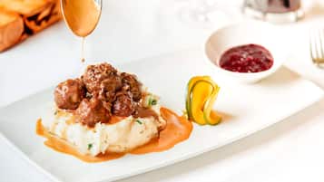 Um prato de almôndegas com molho, purê de batata e uma fatia de abobrinha.