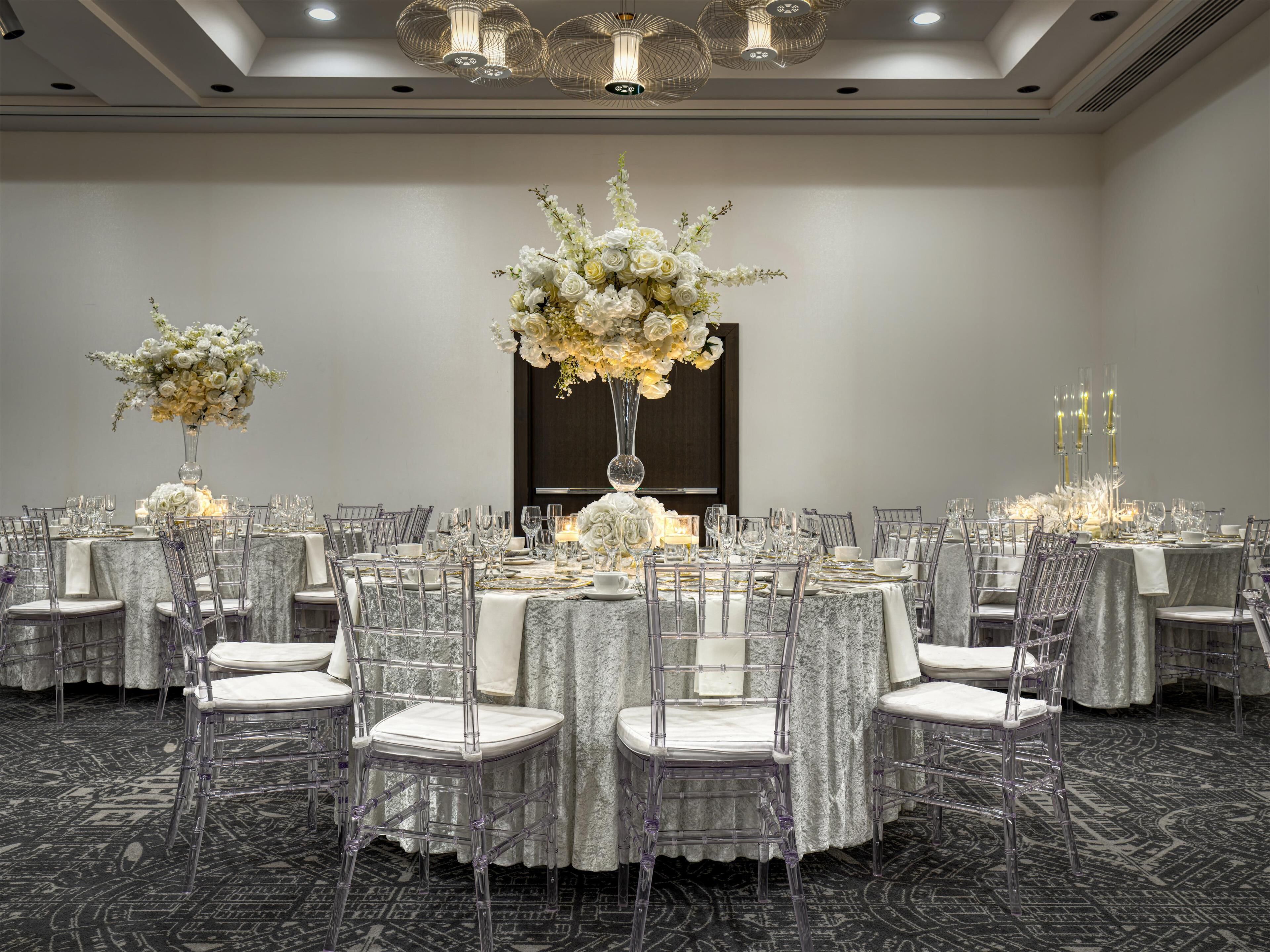 Une salle de banquet avec des tables rondes, des chaises transparentes et des centres de table floraux.