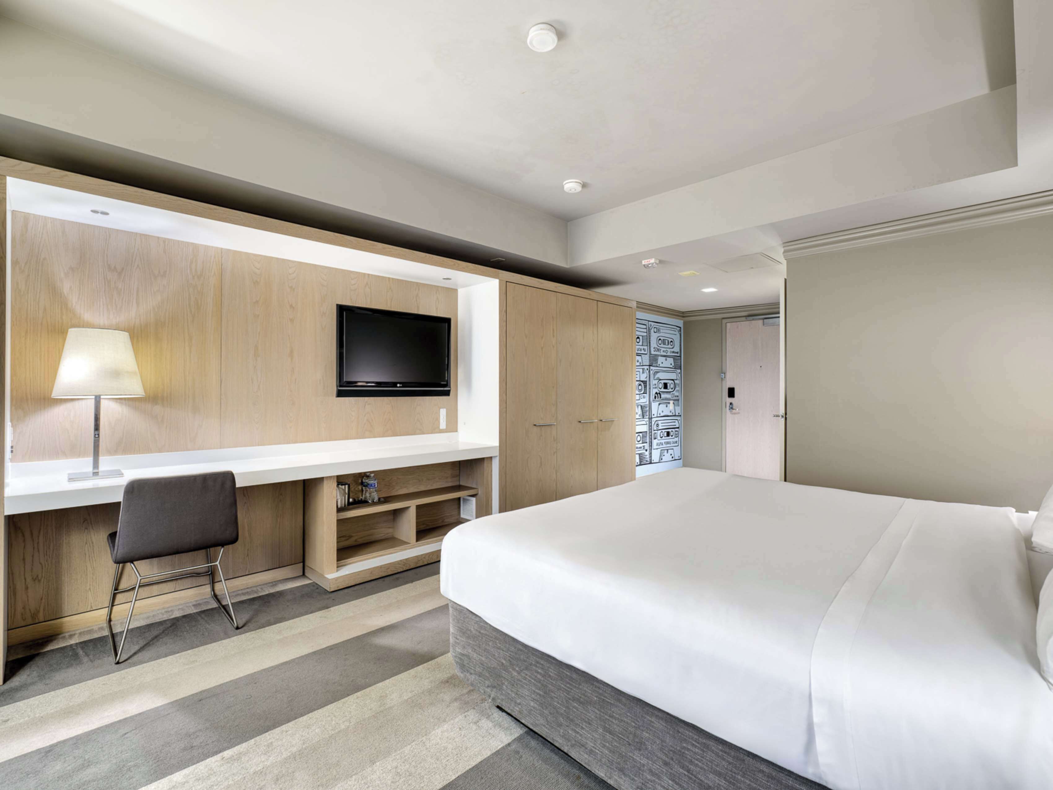 A modern hotel room with a large bed, a desk with a flat-screen TV, and a wall-mounted cabinet.