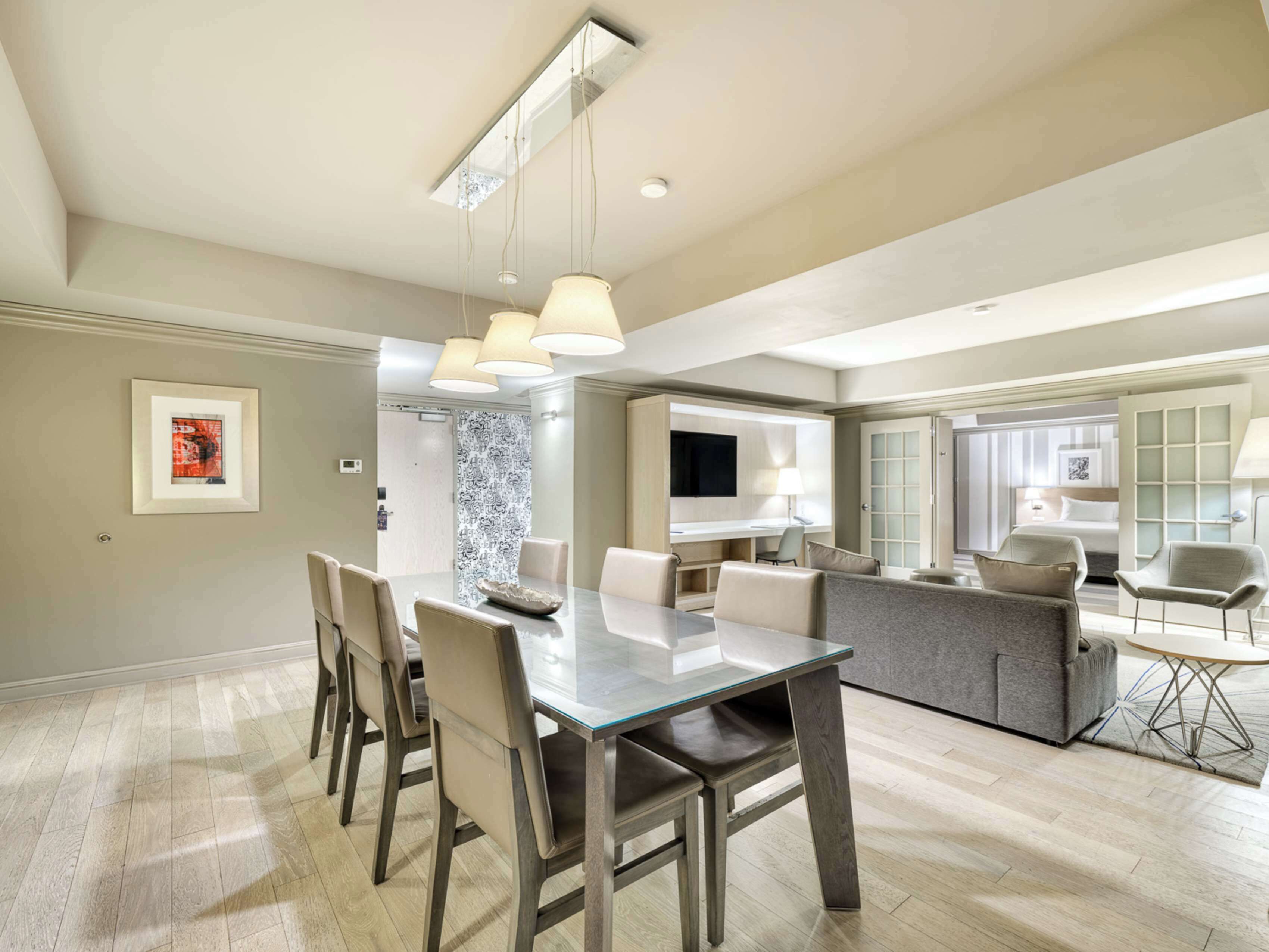 A modern dining area with a glass-top table, multiple chairs, and pendant lighting.
