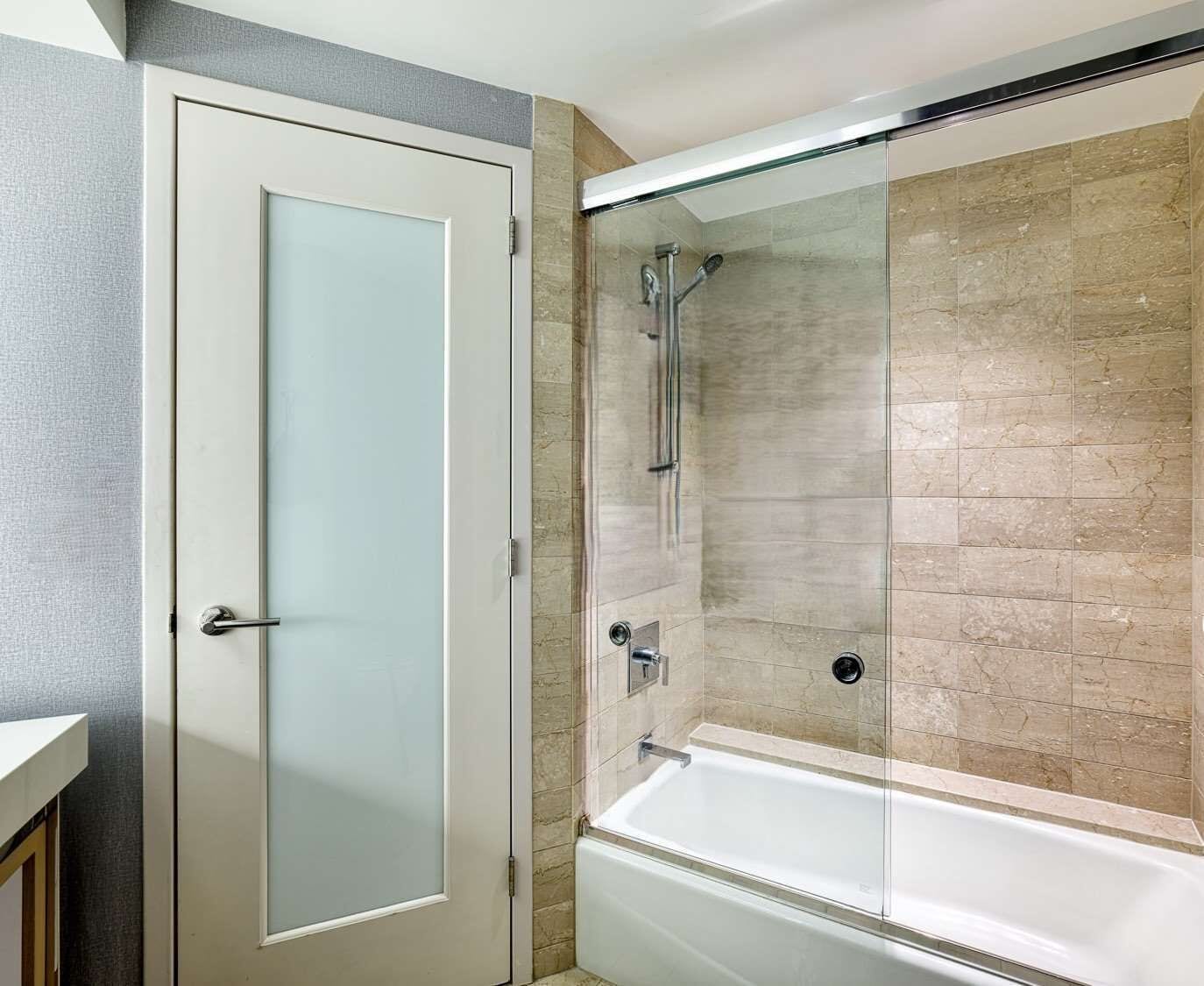 A bathroom with a glass shower enclosure, a white bathtub, and a frosted glass door.