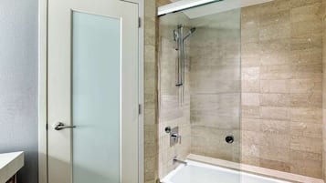 A bathroom with a glass shower enclosure, a white bathtub, and a frosted glass door.