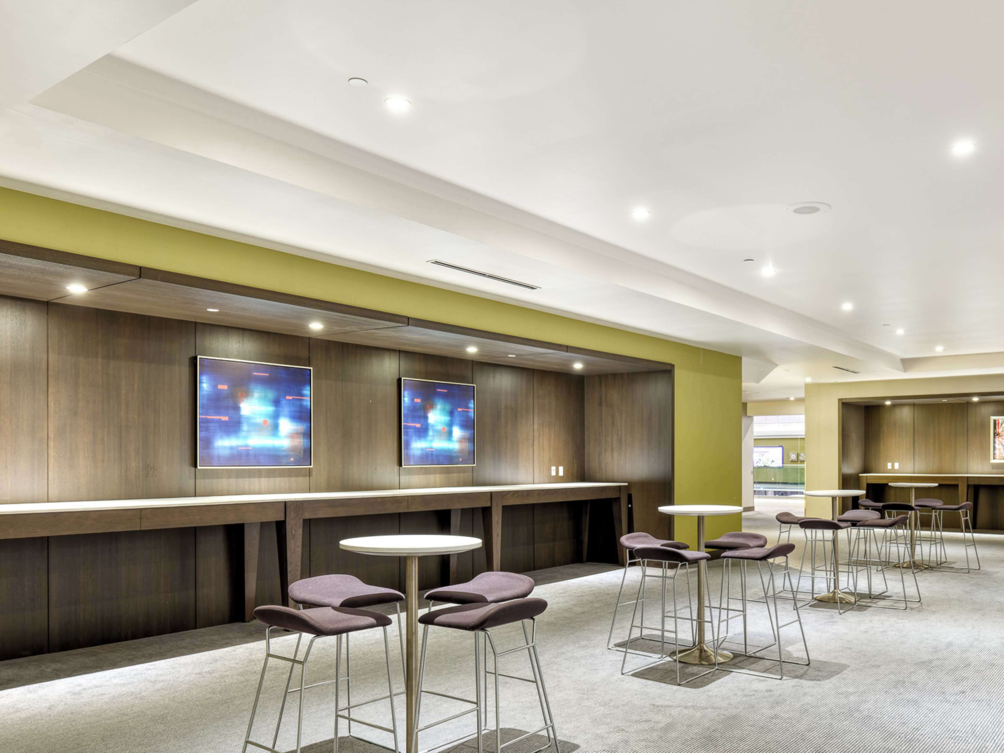 A modern bar area with high stools and a long counter, featuring recessed lighting and a neutral color palette.