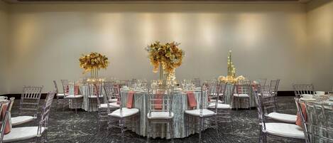 A banquet hall with round tables, clear chairs, and floral centerpieces.