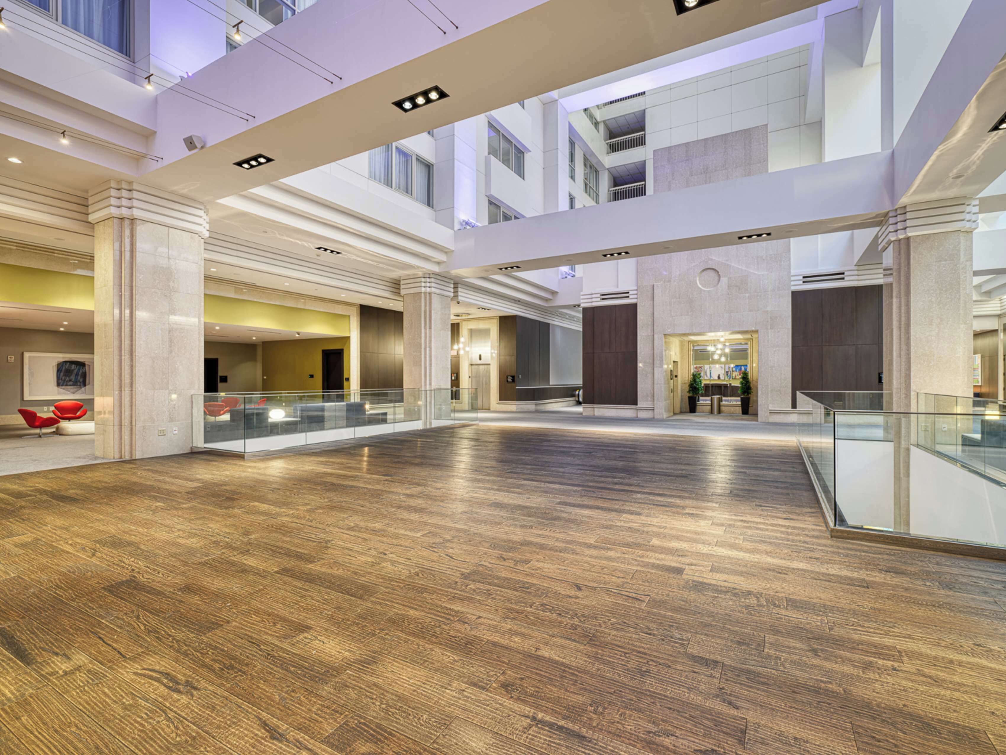 A spacious lobby with a high ceiling, polished wood flooring, and a glass railing overlooking a lower level.