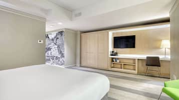 A modern hotel room with a large bed, a desk with a flat-screen TV, and a green chair.