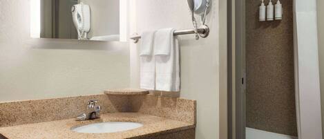 A bathroom with a granite countertop sink, a handheld hair dryer mounted on the wall, and a set of toiletries on the wall.