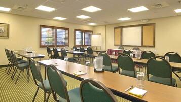 A conference room with multiple tables and chairs, a whiteboard, and windows with blinds.