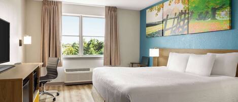 Una habitación de hotel con una cama grande, un escritorio con computadora, una silla y una ventana con cortinas.