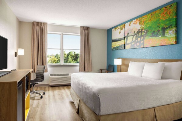 A hotel room with a large bed, a desk with a computer, a chair, and a window with curtains.