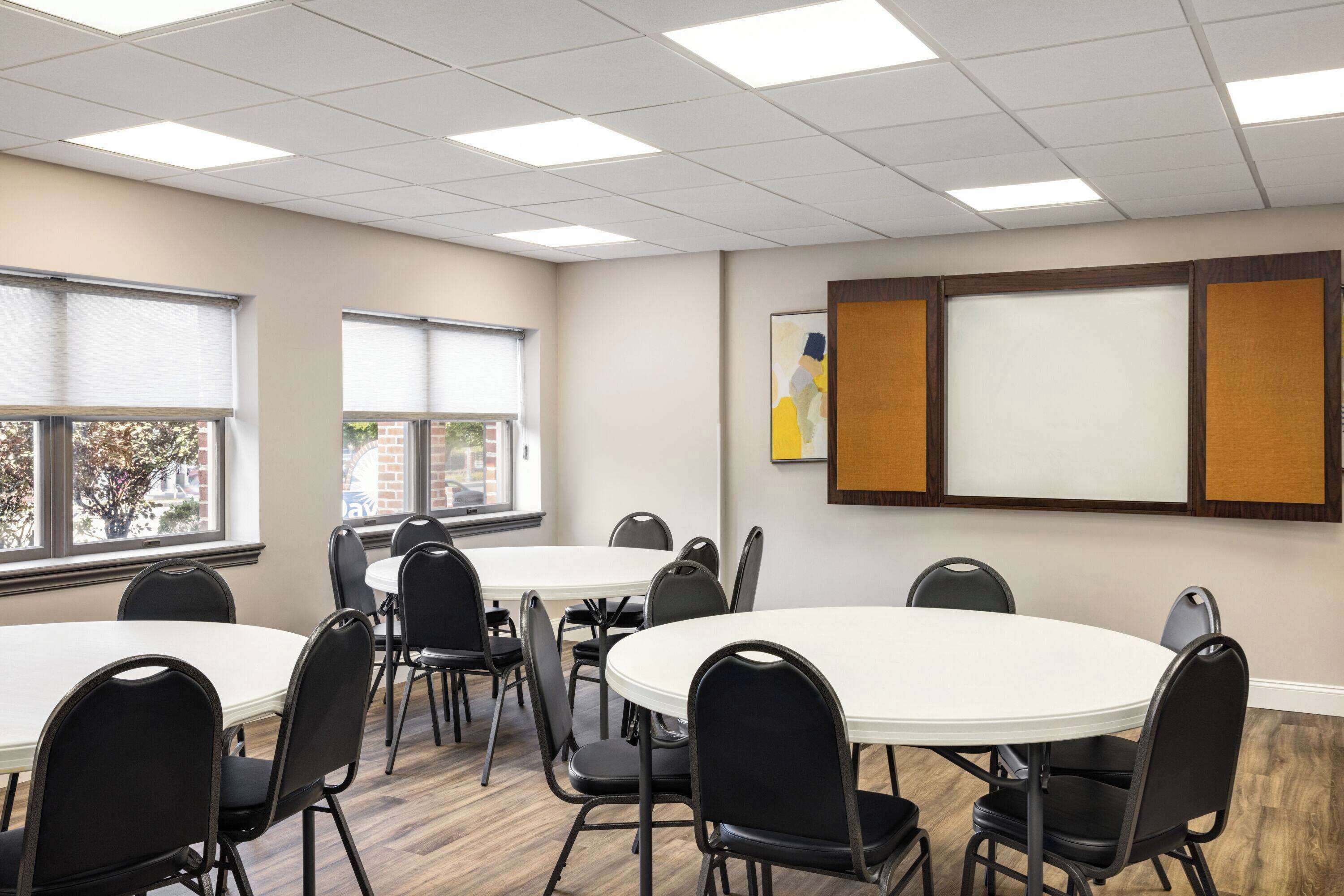 A conference room with round tables and chairs, large windows, and a whiteboard on the wall.