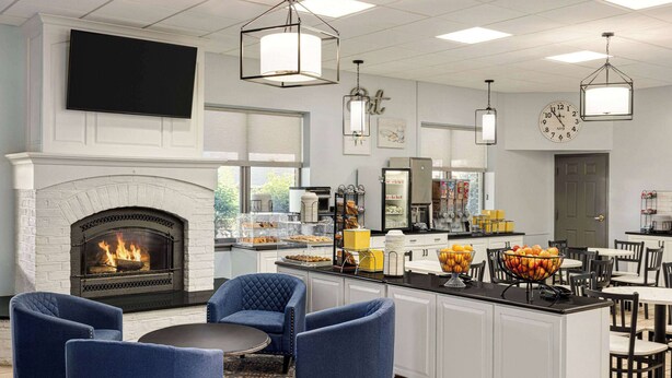 A modern kitchen with a fireplace, blue chairs, a dining area, and a large island with fruit bowls. - Days Inn by Wyndham Hershey (Hershey)