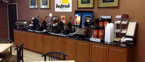 A breakfast counter with waffle makers, coffee machines, and a 'Daybreak Breakfast' sign.
