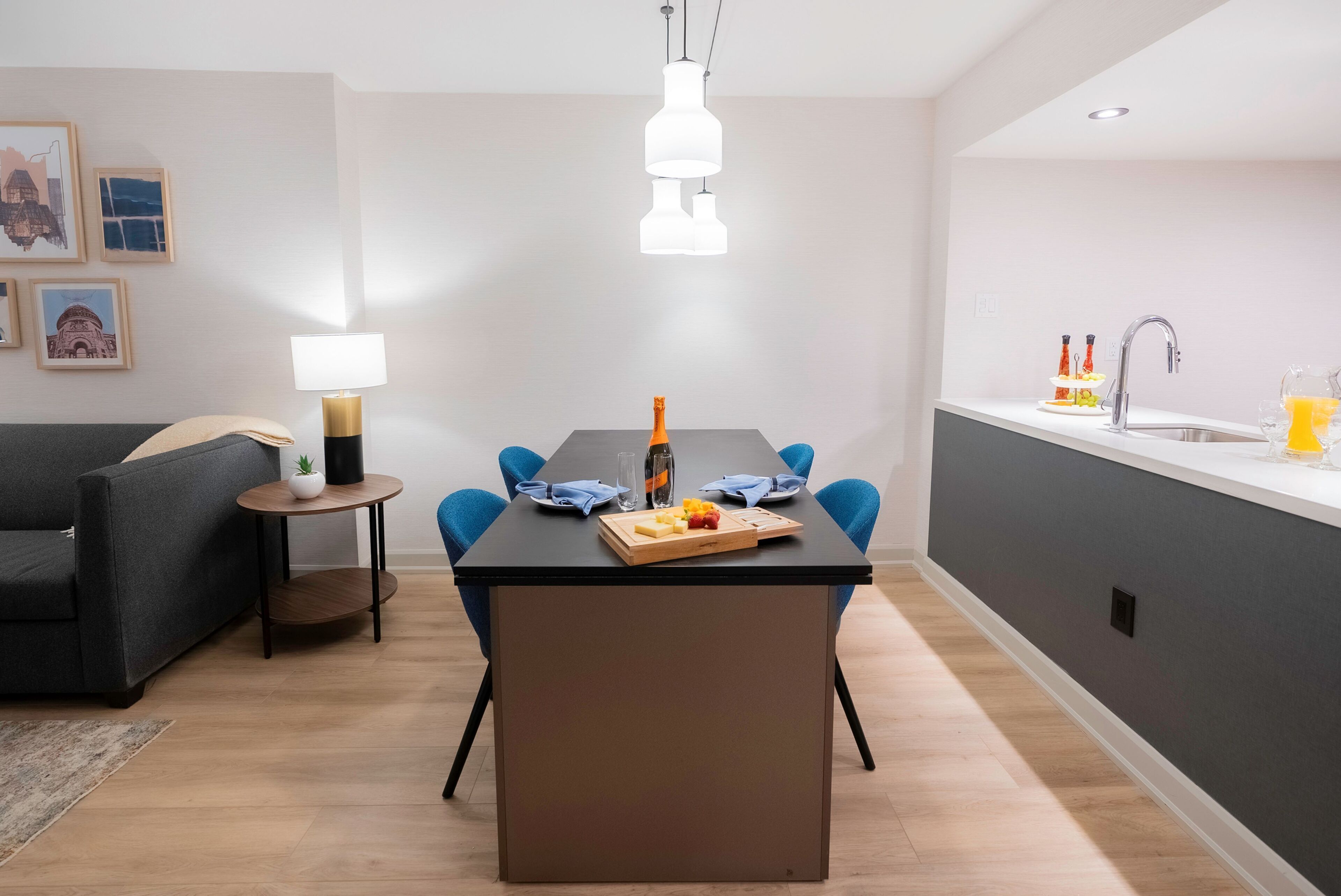 A modern kitchen with a dining area, featuring a black table, blue chairs, and a pendant light.