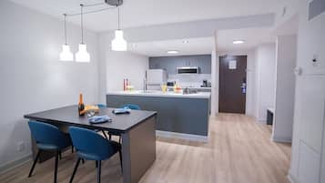 A modern kitchen with a central island, a dining area with blue chairs, and a hallway leading to a door.